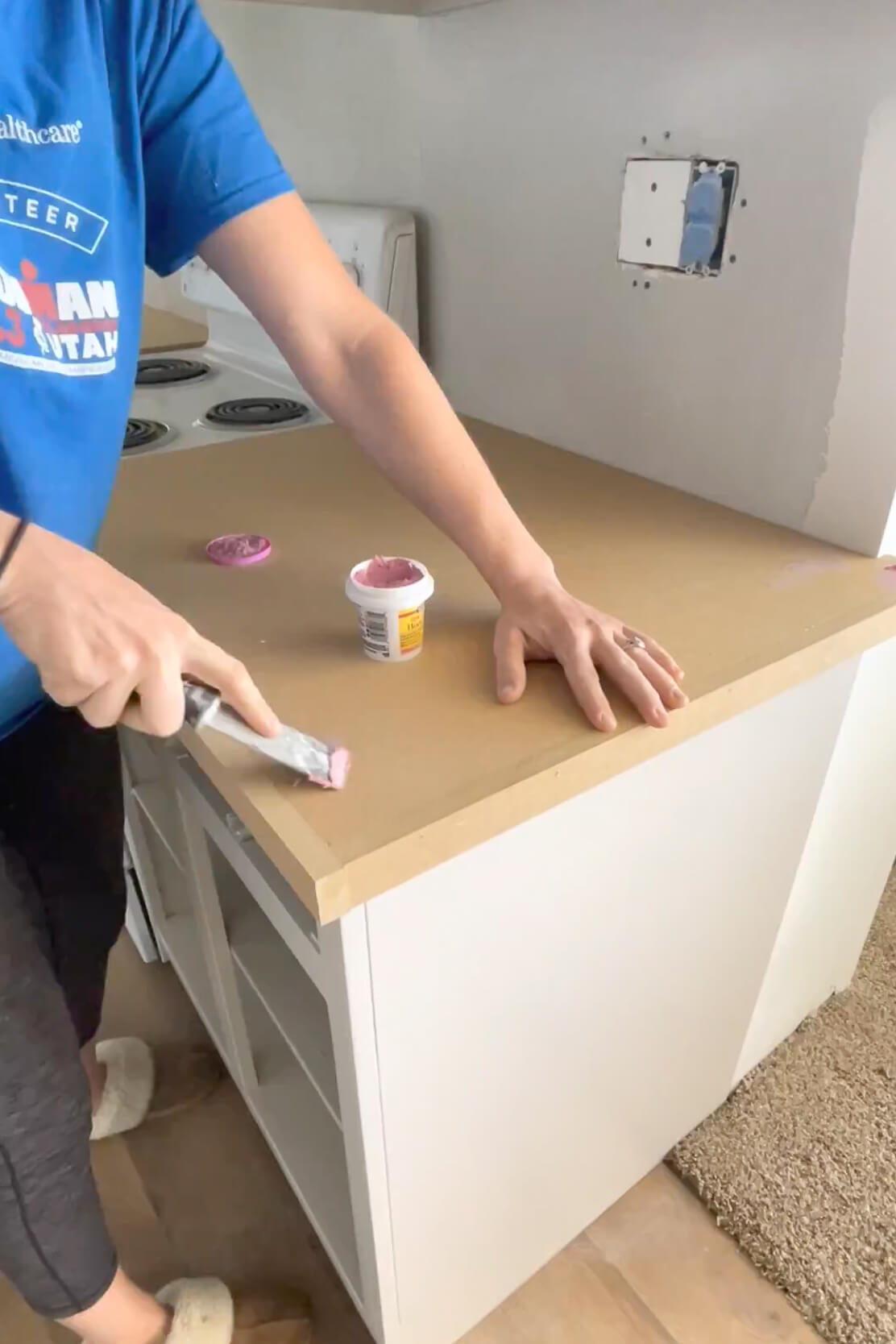 Using wood filler to fill in seams and nail holes in a DIY kitchen countertop.